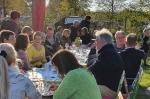 Ca. 20 Menschen sitzen an einer langen Tafel in einem Kaffeegarten