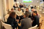 ca. 15 Menschen sitzen in 2 Stuhlkreisen vor einer Leinwand
